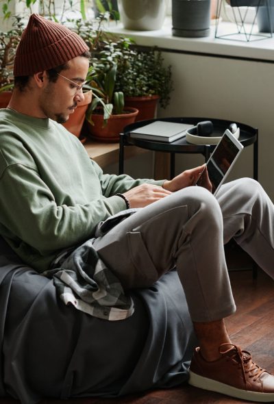 Young serious webdesigner with laptop concentrating on network Young serious webdesigner with laptop concentrating on network while sitting in comfortable armchair in office with many green plants